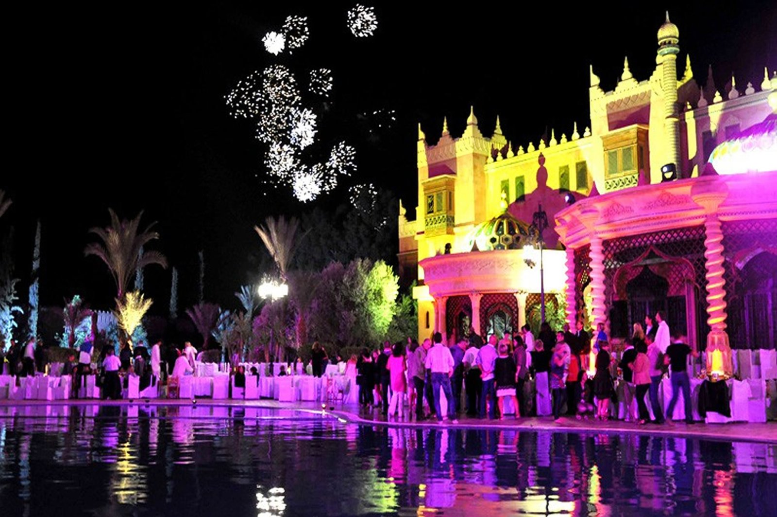 Fuegos artificiales sobre el recinto iluminado de Chez Ali y visitantes por la noche
