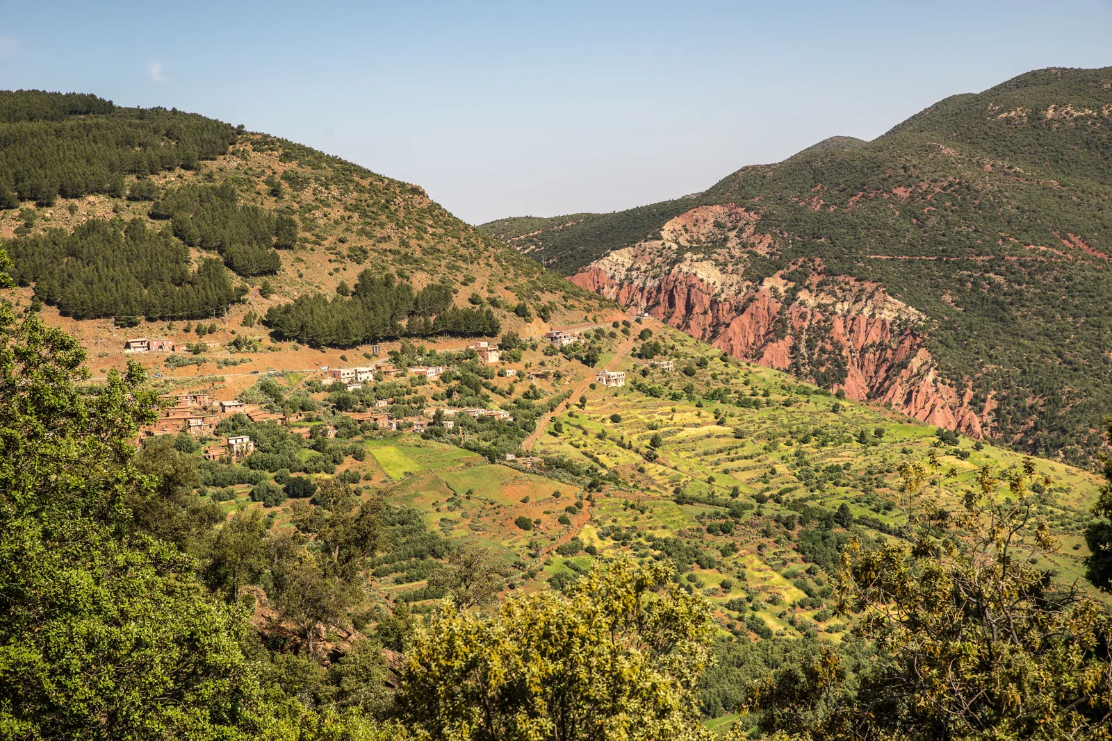 Terraced green fields and hillside homes beneath red cliffs near Imlil and Asni