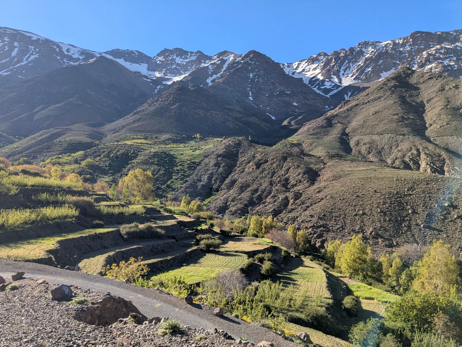 Terraced fields and trees beneath snow-dusted Atlas Mountain peaks near Imlil and Asni