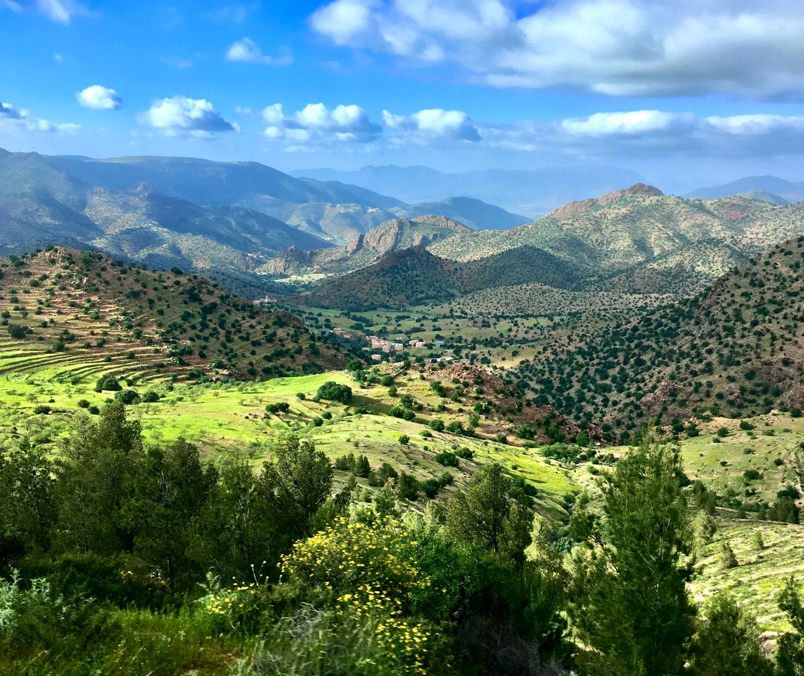 Green valleys and terraced fields surrounded by Atlas Mountains beneath a cloudy blue sky