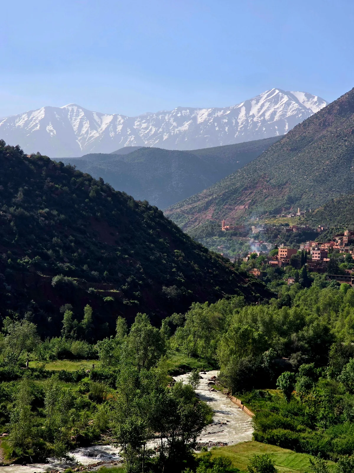 River winding through a green valley beneath snow-covered Atlas Mountains