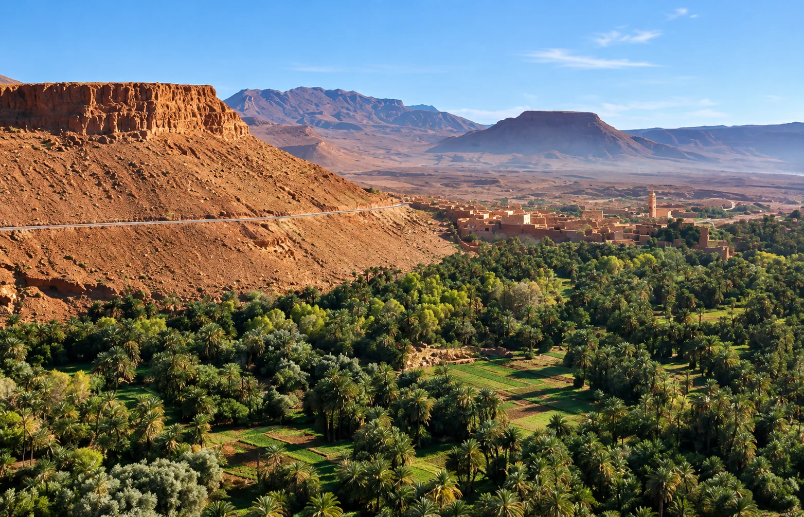 Palm oasis and traditional village beneath rocky mountains