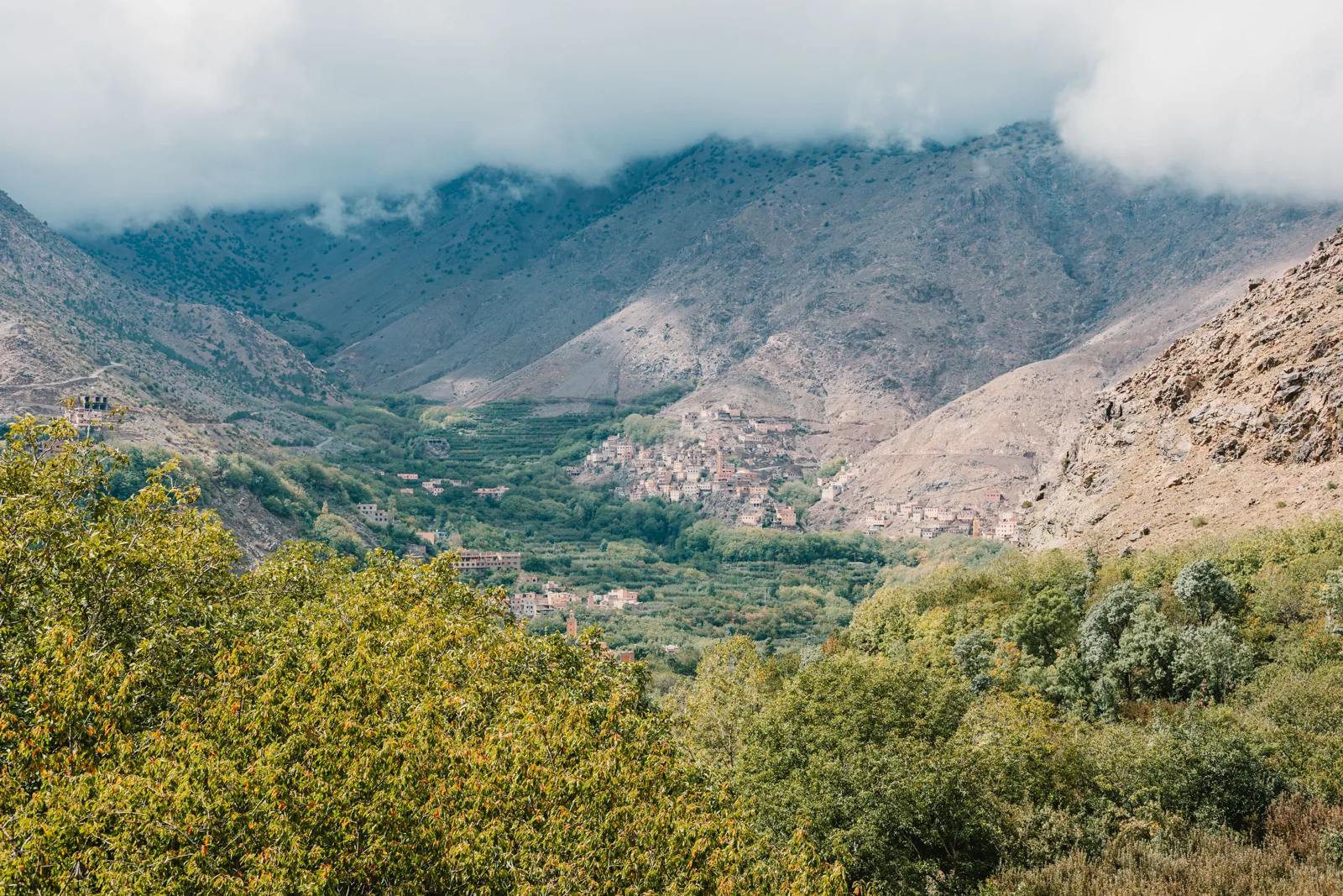 Green valley and mountain village beneath low clouds in the Atlas Mountains